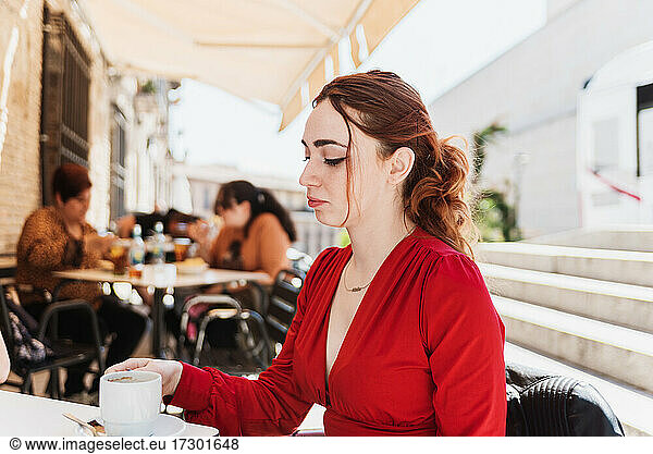 Young red-haired woman in a red blouse having a coffee on a terrace