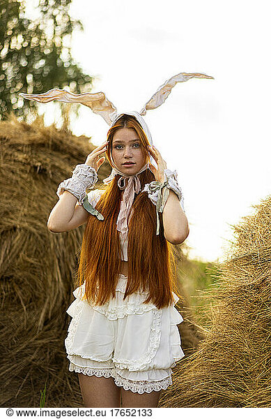 Young redhead woman adjusting rabbit costume ears standing at farm