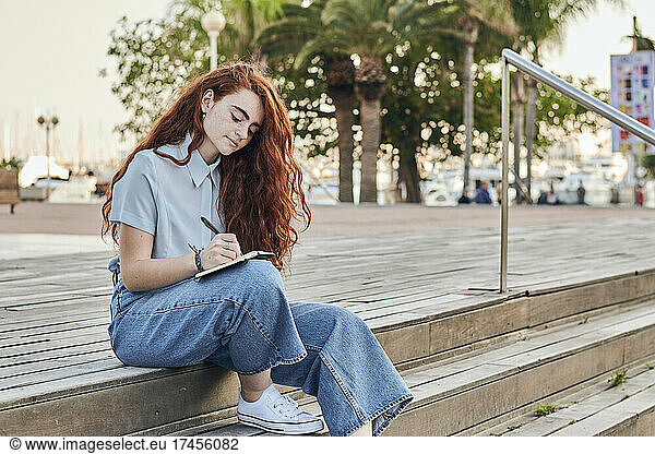 Young redhead woman writes in a notebook outdoors