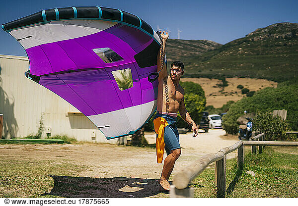 Young shirtless man holding hydrofoil at beach on sunny day