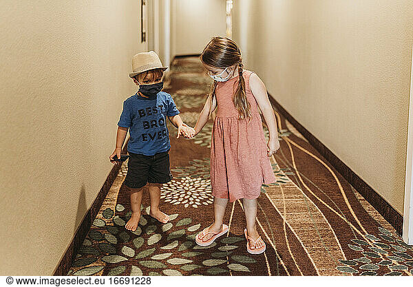 Young siblings wearing masks walking through hotel hallway together