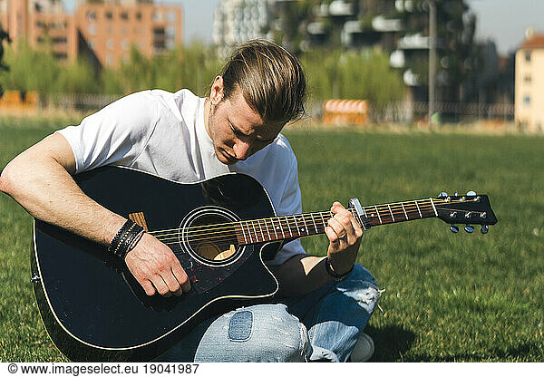 Young singer play the guitar in a garden during a sunny day