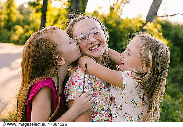 Young sisters laugh  hug and kiss in golden light