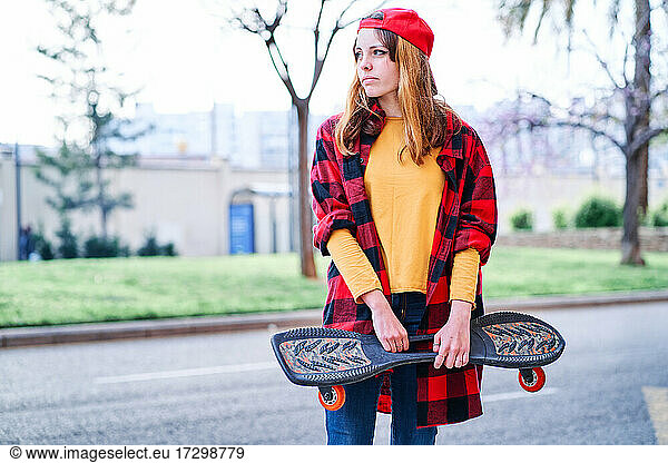 Young Skater Girl in Plaid Shirt and Red Cap in the City. Copy space
