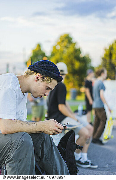 Young skater in skatepark using his smartphone