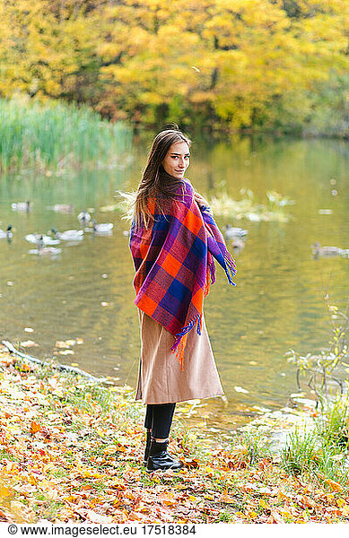 Young smiling brunette girl enjoying walking in park wrapped in plaid