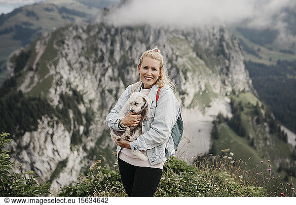 Young smiling female hiker with dog on viewpoint