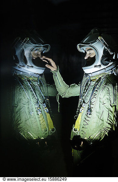 Young spaceman touching his reflection in the dark