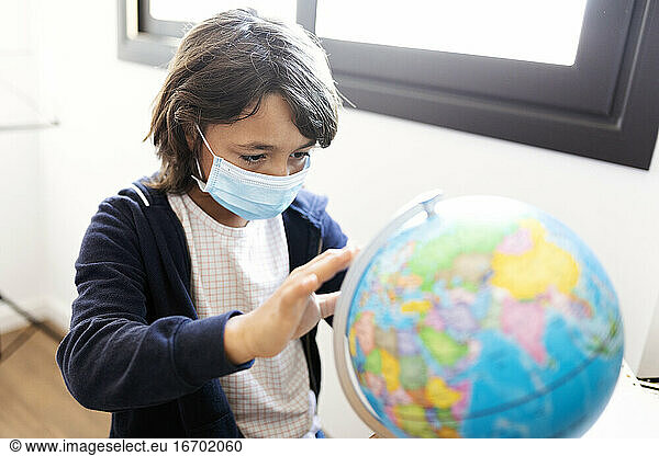 Young spanish boy holding a desk globe wearing a medical mask