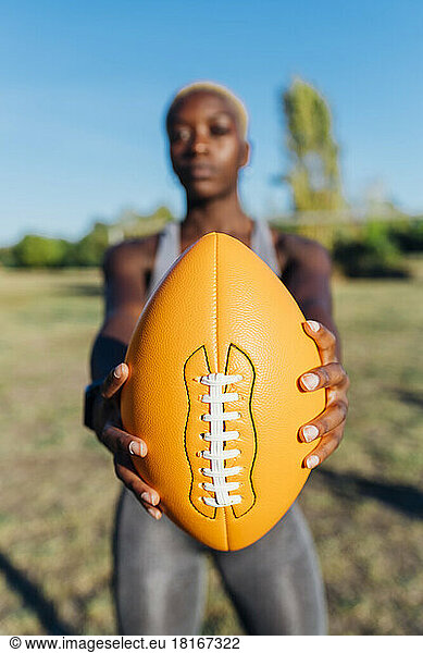 Young sports player showing American football on sunny day