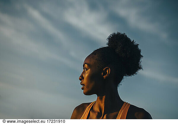 Young sportswoman looking away against sky during sunset