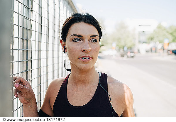Young sportswoman looking away while listening music through in-ear headphones on bridge