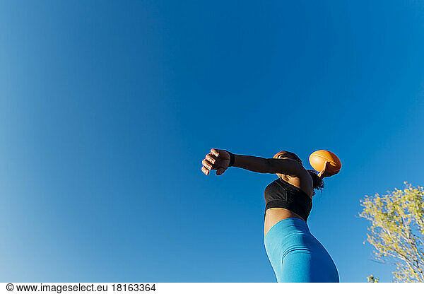 Young sportswoman throwing American football on sunny day