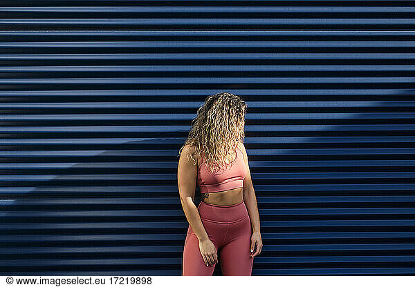 Young sportswoman with curly hair standing in front of blue wall
