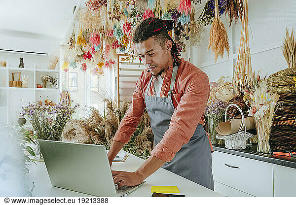 Young store owner using laptop at desk in flower shop