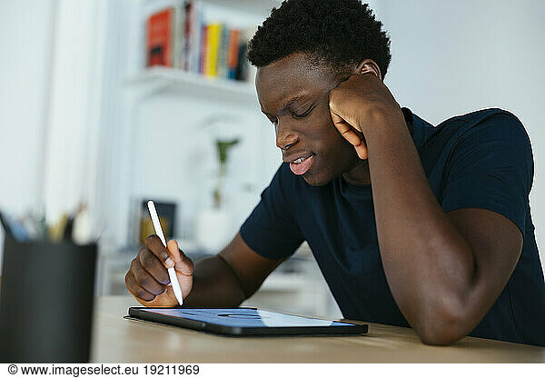 Young student studying and writing on tablet PC at desk