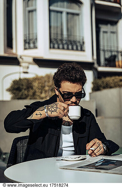 Young tattooed guy smoking a cigar on a terrace while having a coffee