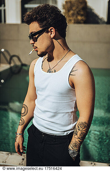 Young tattooed guy with sunglasses smoking a cigar on a terrace