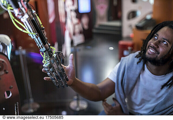 Young tech developer shaking hand with robotic arm at workshop