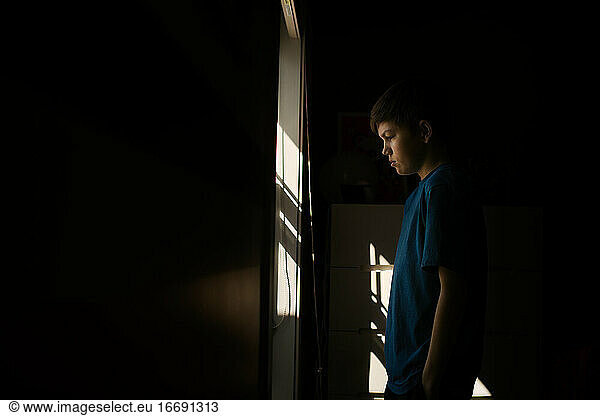Young teen boy looking out the window during isolation