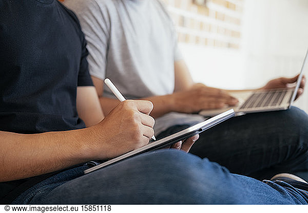 Young teenage men using computer and tablet for online learning.