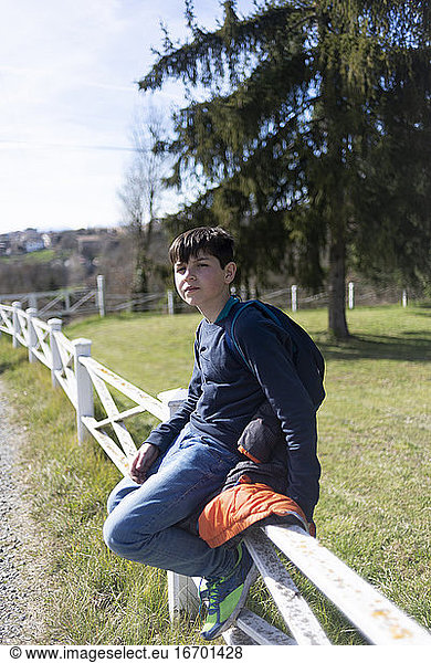 Young teenager male sitting on countryside fence looking camera