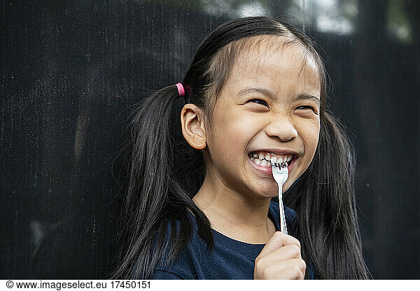young Thai girl biting on fork