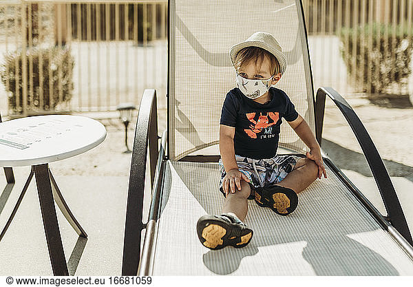 Young toddler boy with mask on sitting by pool in Palm Springs