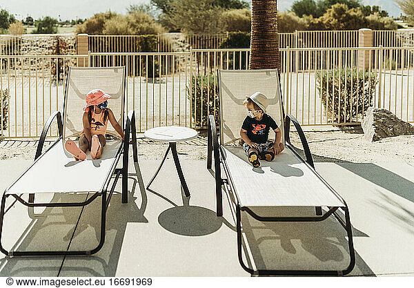 Young toddler siblings with mask on sitting by pool in Palm Springs