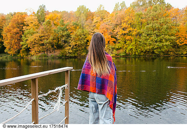 Young trendy girl wrapped in a colorful plaid in park back view