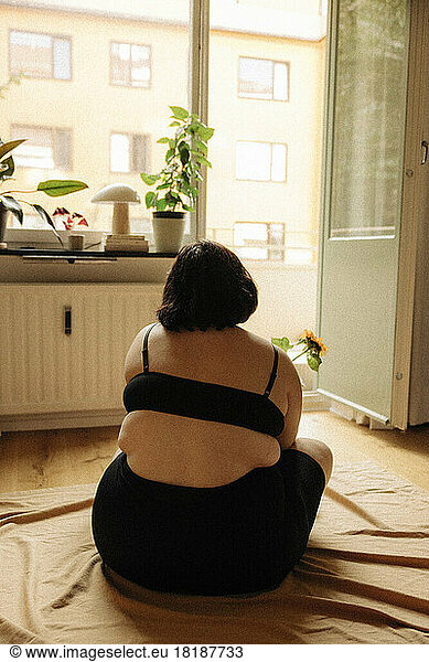 Young voluptuous woman in black lingerie sitting against door at home
