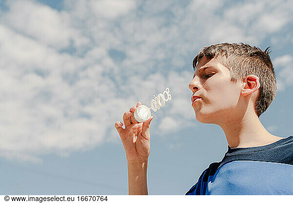 Young white boy blowing a soap bubble outdoors with sky at background