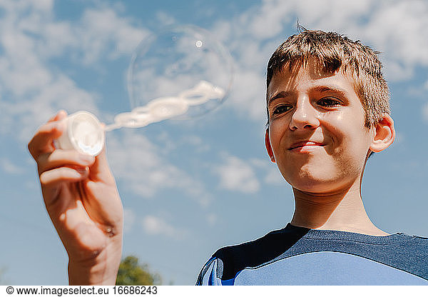 Young white boy looking a soap bubble outdoors with sky at background