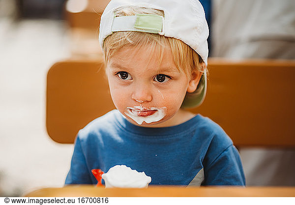 Young white child eating ice cream with dirty mouth and cap