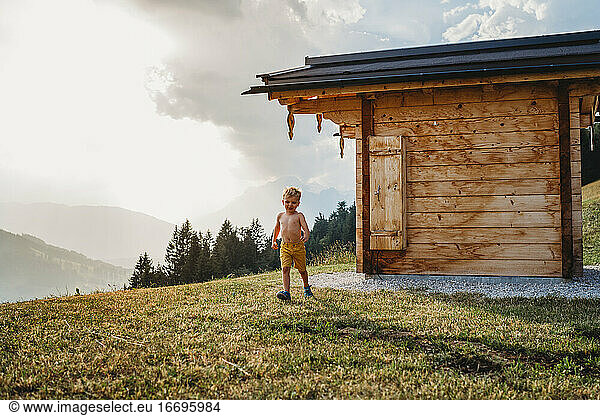 Young white child running in mountains behind wooden house
