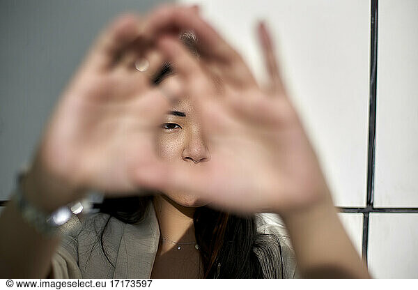 Young woman against wall while looking through hand