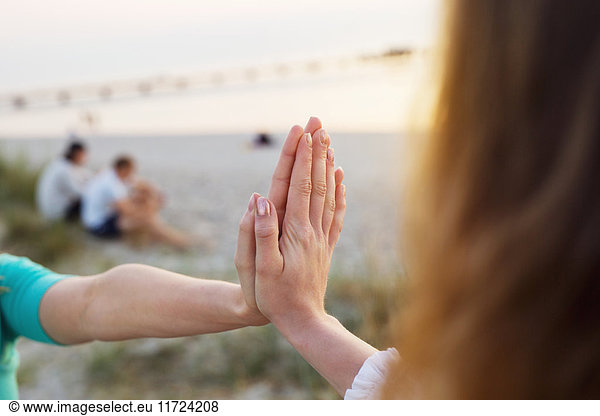Young woman and teenage girl (16-17) touching hands  young men sitting on beach at sunset