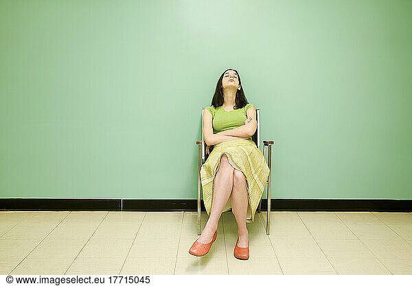 Young Woman Asleep In A Chair In Front Of A Green Wall
