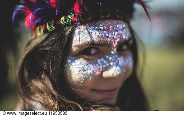 Young woman at a summer music festival face painted  wearing feather headdress  looking at camera.