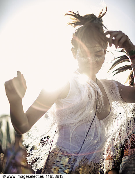 Young woman at a summer music festival in a white vest top with fringes with arms raised  dancing among the crowd.