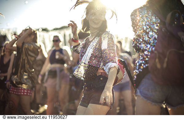 Young woman at a summer music festival wearing feather headdress  dancing among the crowd.