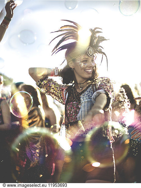 Young woman at a summer music festival wearing feather headdress  dancing among the crowd.