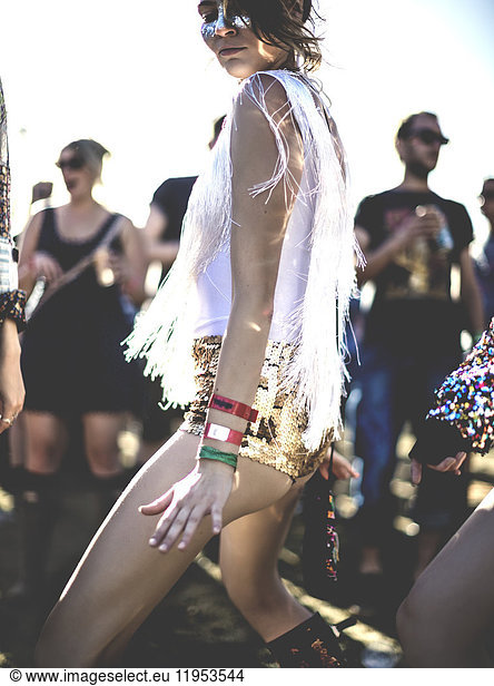 Young woman at a summer music festival wearing golden sequinned hot pants  dancing among the crowd.