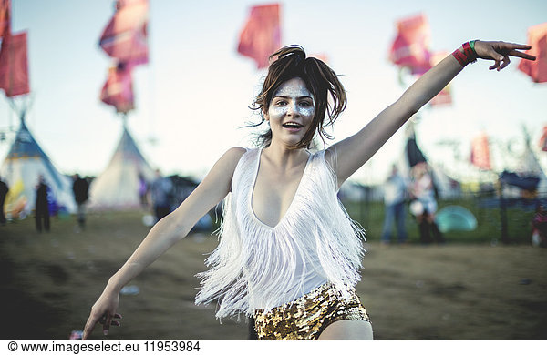 Young woman at a summer music festival wearing golden sequinned hot pants  face painted  smiling at camera.