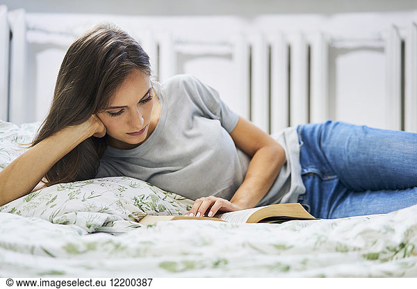 Young woman at home lying in bed reading book