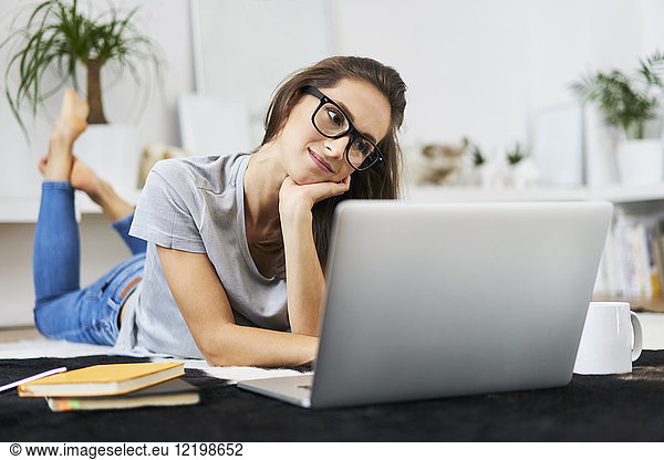 Young woman at home lying on the floor using laptop