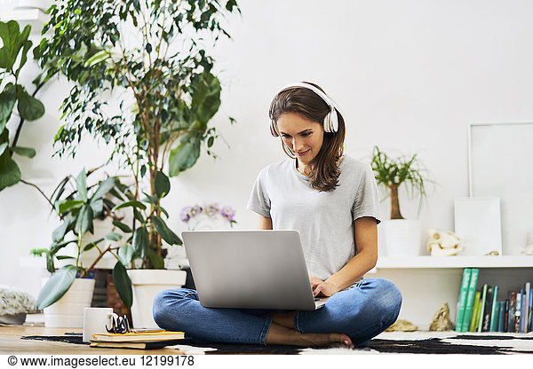 Young woman at home sitting on the floor using laptop and listening to music