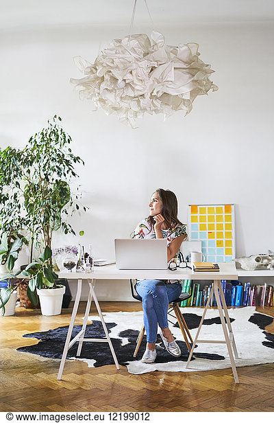 Young woman at home with laptop on desk looking sideways
