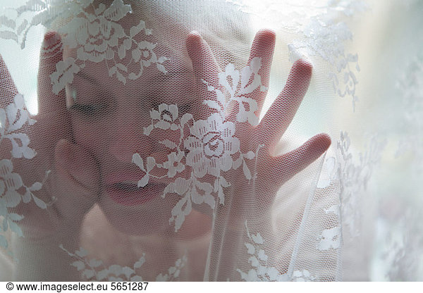 Young woman behind lace curtain