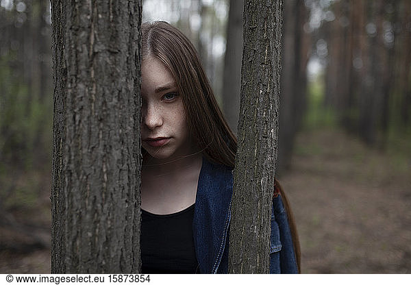 Young woman behind tree trunks in forest